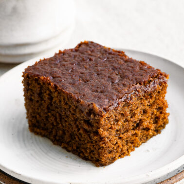 Slice of gingerbread cake on a plate next to a cup of coffee.