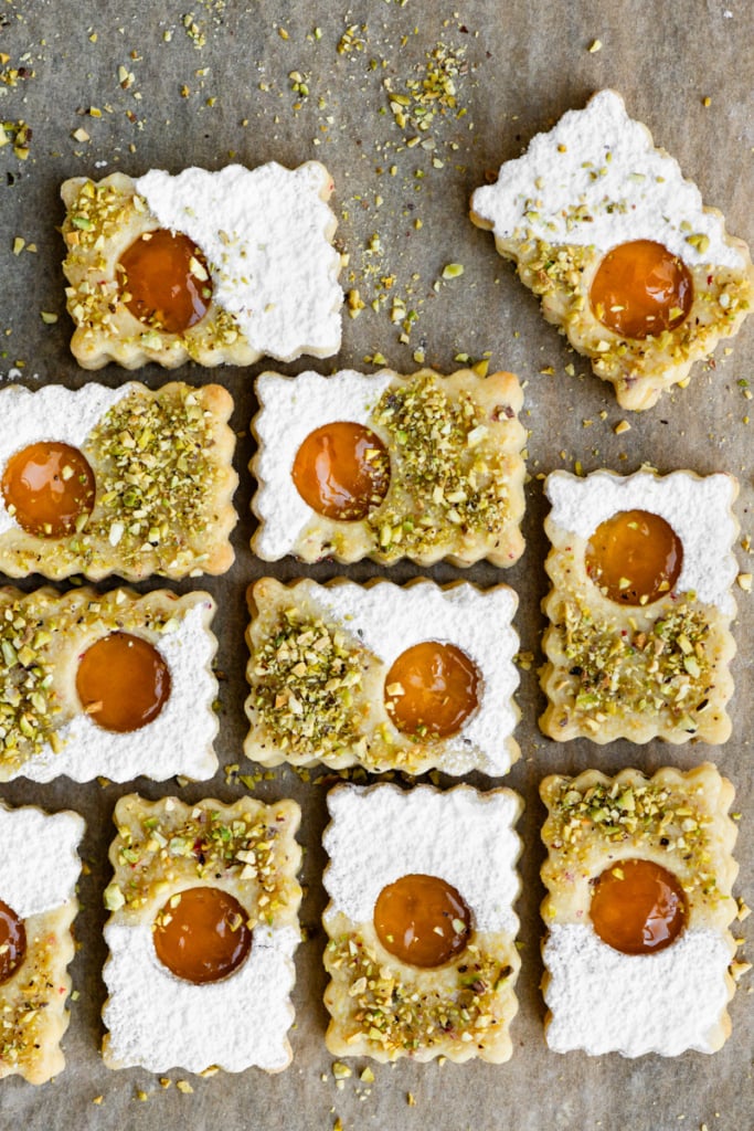 Rectangular linzer cookies topped with powdered sugar and pistachios placed on parchment paper.