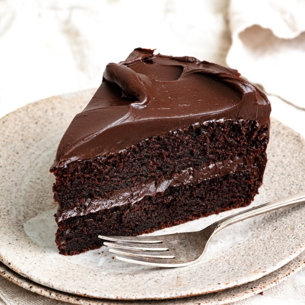 Slice of chocolate cake with chocolate ganache frosting topped on a plate with a fork.