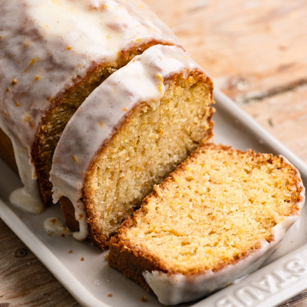 Vanilla glazed orange loaf cake on a serving platter with two slices cut.