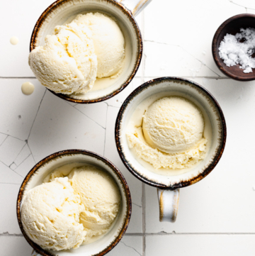 Overhead view of three coffee mugs filled with scoops of ice cream drizzled with honey.