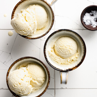 Overhead view of three coffee mugs filled with scoops of ice cream drizzled with honey.