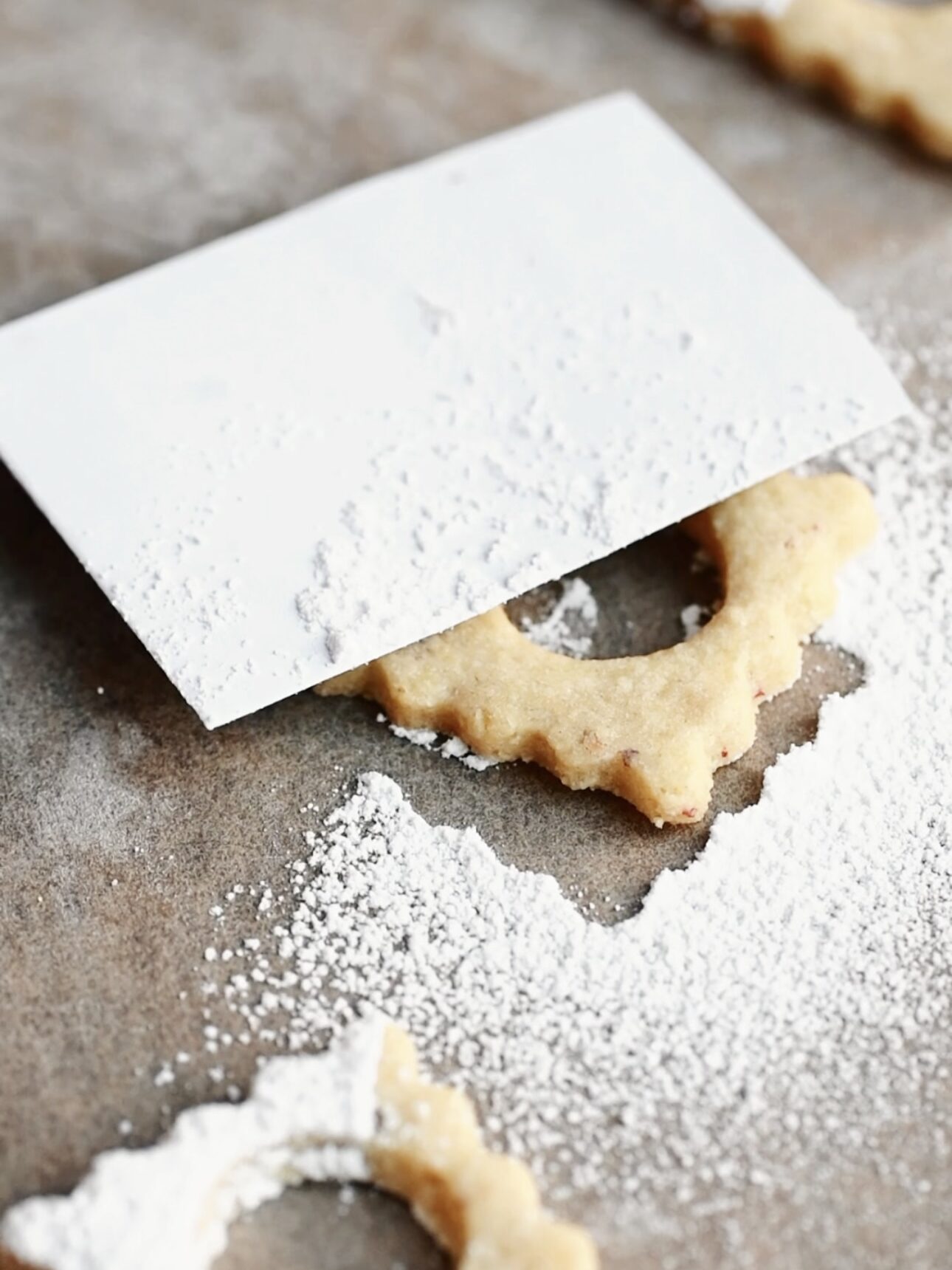 Baked linzer cookie top covered halfway with a piece of paper and powdered sugar all around.