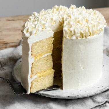 Three layer 6-inch cake with vanilla frosting and lemon curd filling with a slice being pulled away.