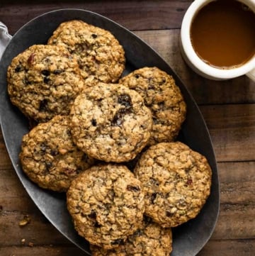 Oval plate filled with a stack of oatmeal cookies next to a cup of coffee.