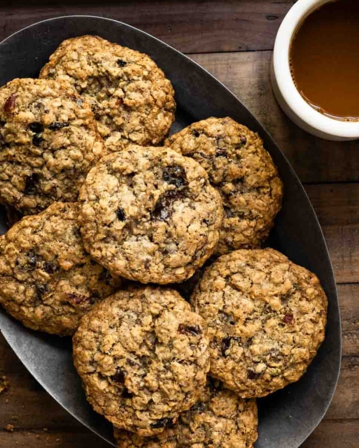 Oval plate filled with a stack of oatmeal cookies next to a cup of coffee.