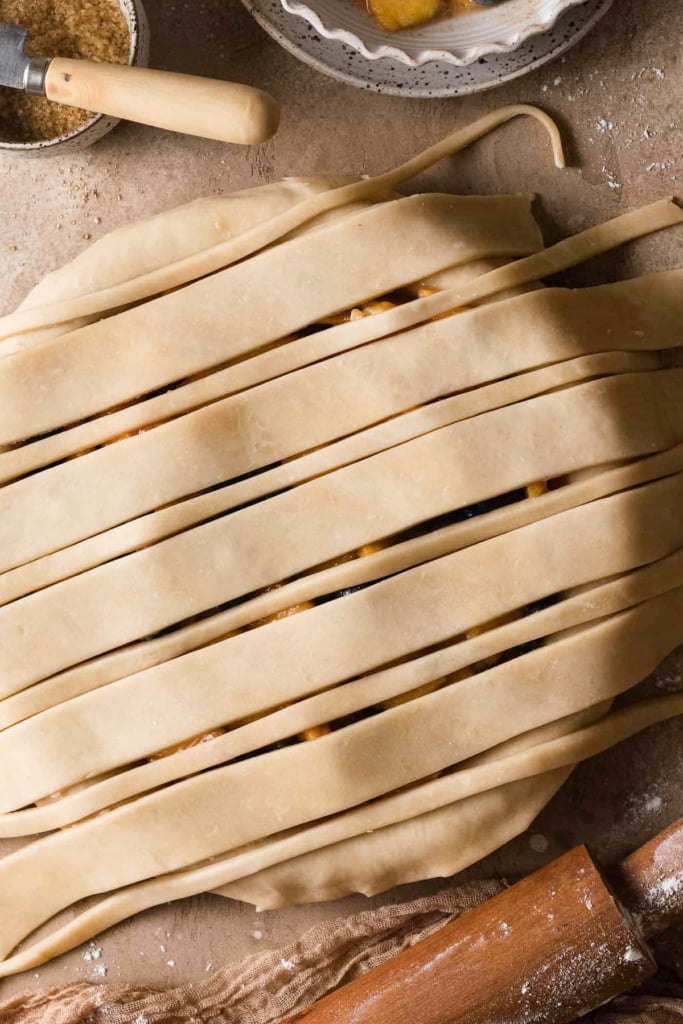 Overhead view of an unbaked pie with strips of lattice pie dough in different thicknesses across the top.