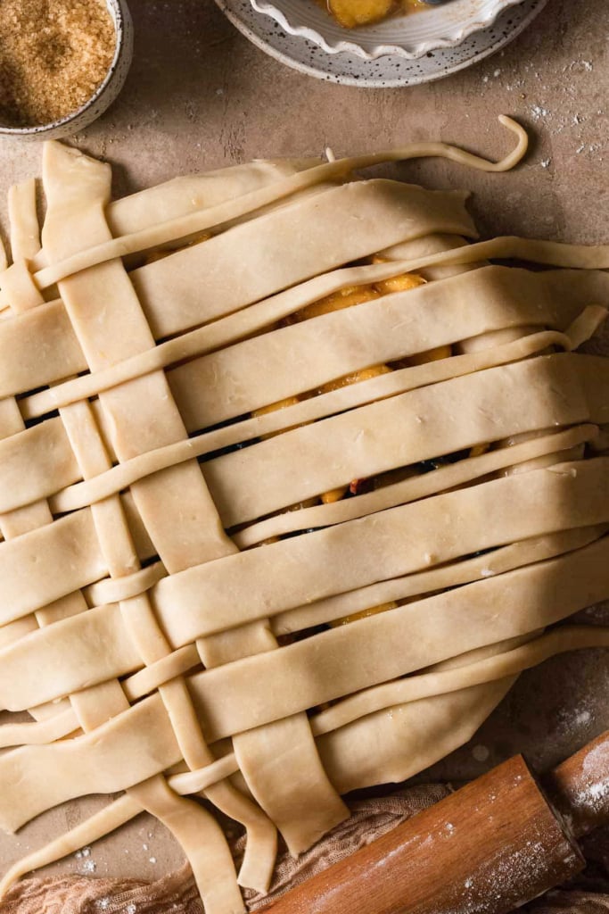 Overhead view of an unbaked pie with strips of lattice pie dough in different thicknesses across the top. With a second layer partially weaved through.