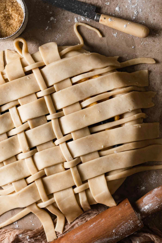 Overhead view of an unbaked pie with strips of lattice pie dough in different thicknesses across the top. With a second layer partially weaved through.