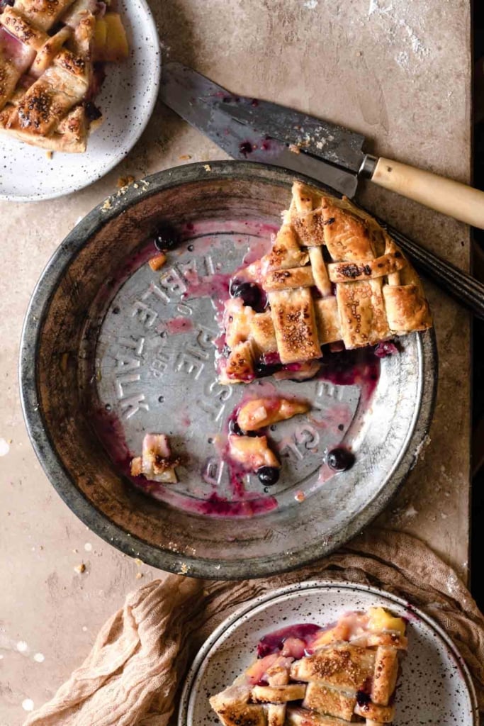 Three slices of peach and blueberry pie with one in a pie dish and two on plates.