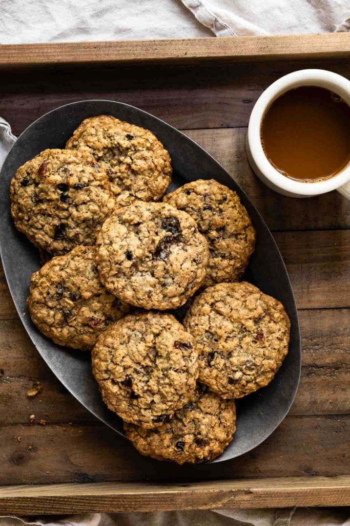 Oval plate filled with a stack of oatmeal cookies next to a cup of coffee.