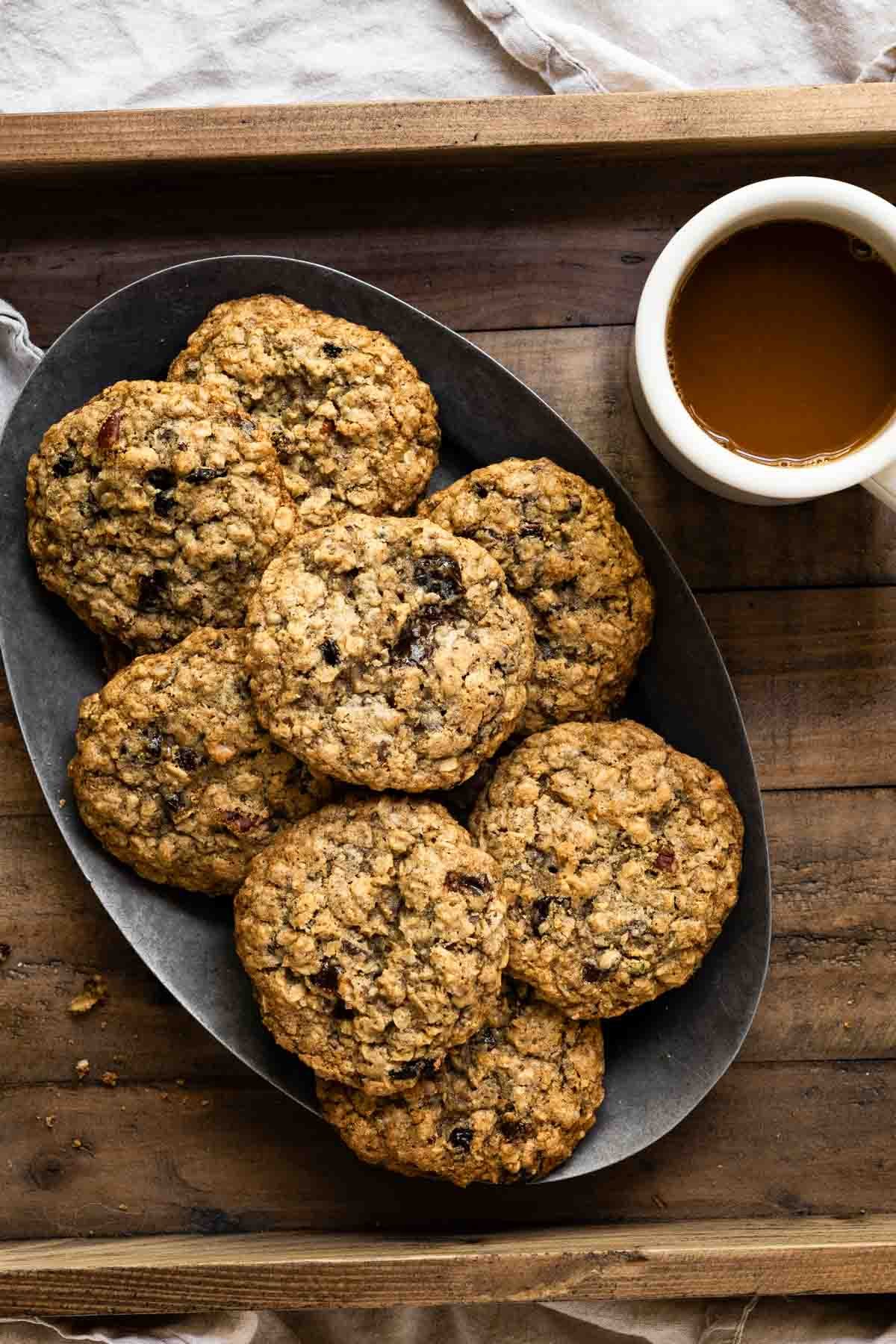 Oval plate filled with a stack of oatmeal cookies next to a cup of coffee.
