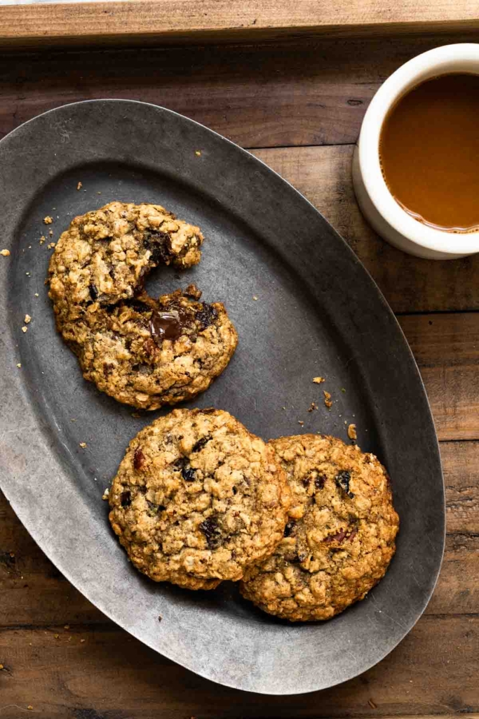 Three oatmeal cookies on an oval plate next to a cup of coffee.