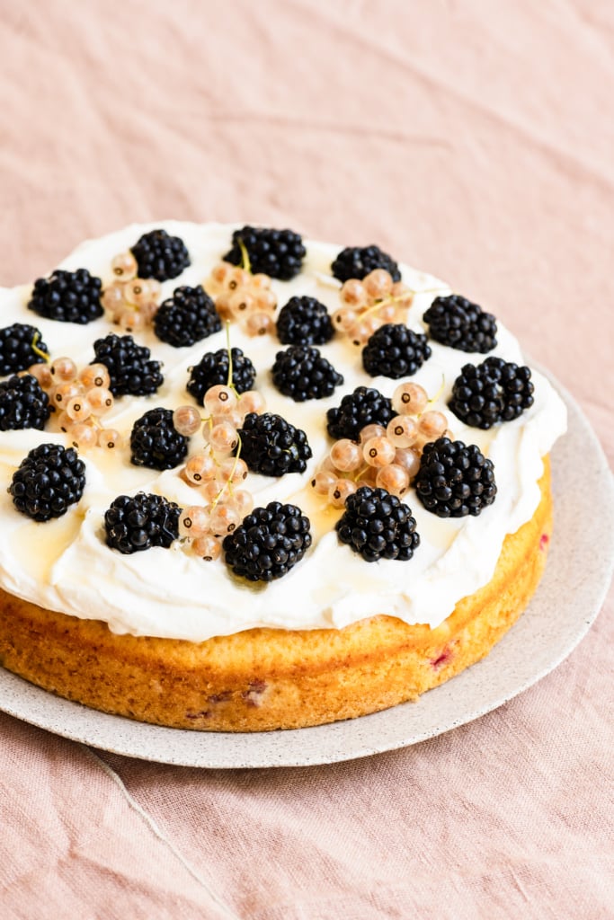 One layer cake topped with blackberries and currants on whipped cream.