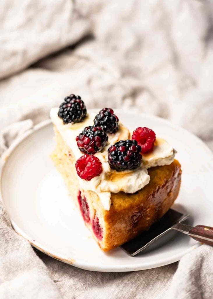 Slice of cake topped with whipped cream and berries on a plate.