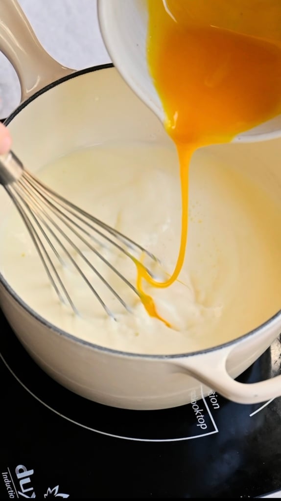 Egg yolks being whisked into cream in a saucepan.