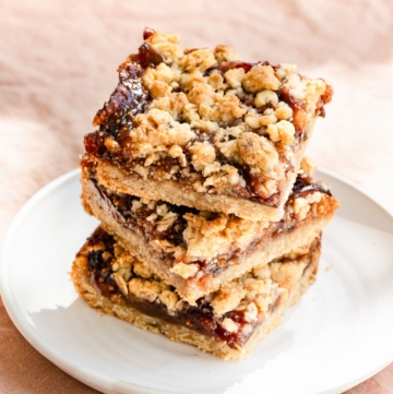 Three square oat crumble bars filled with jam stacked on a plate.