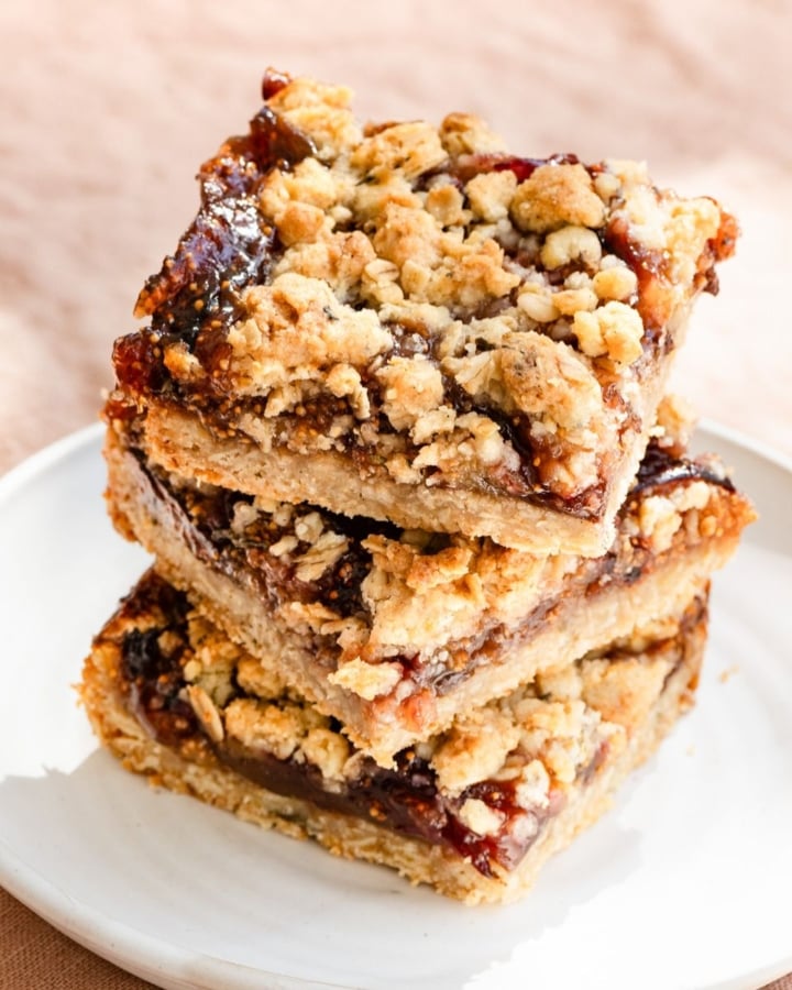 Three square oat crumble bars filled with jam stacked on a plate.