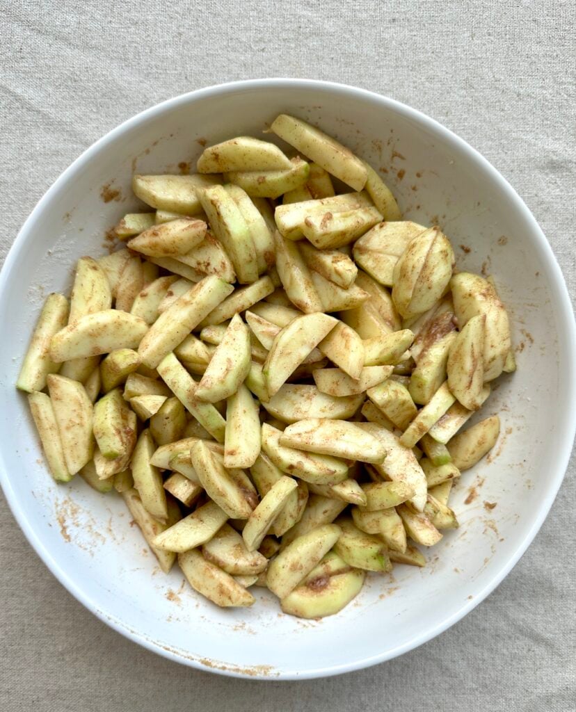 Cooked apple sliced tossed in sugar and spices in a bowl.