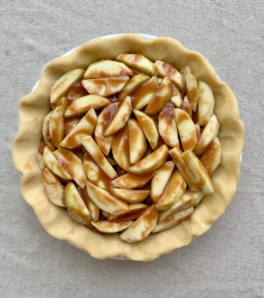 Apple sliced covered in caramel inside an unbaked pie crust.