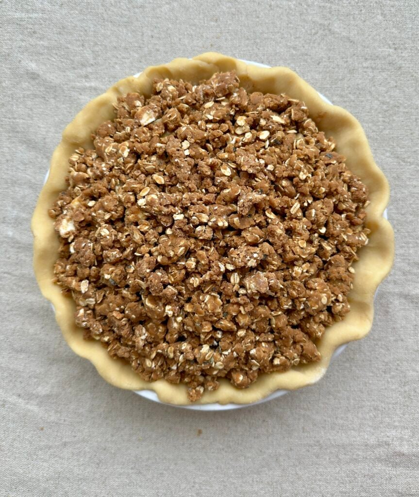 Oat crumble topping packed onto an unbaked apple pie.