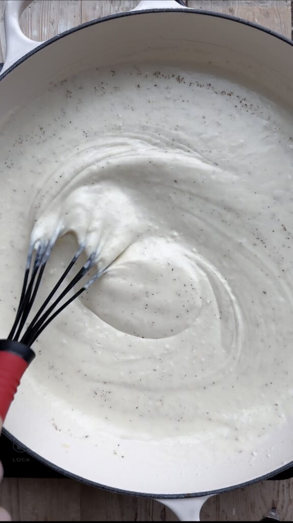 A whisk stirring seasoned milk in a pan.