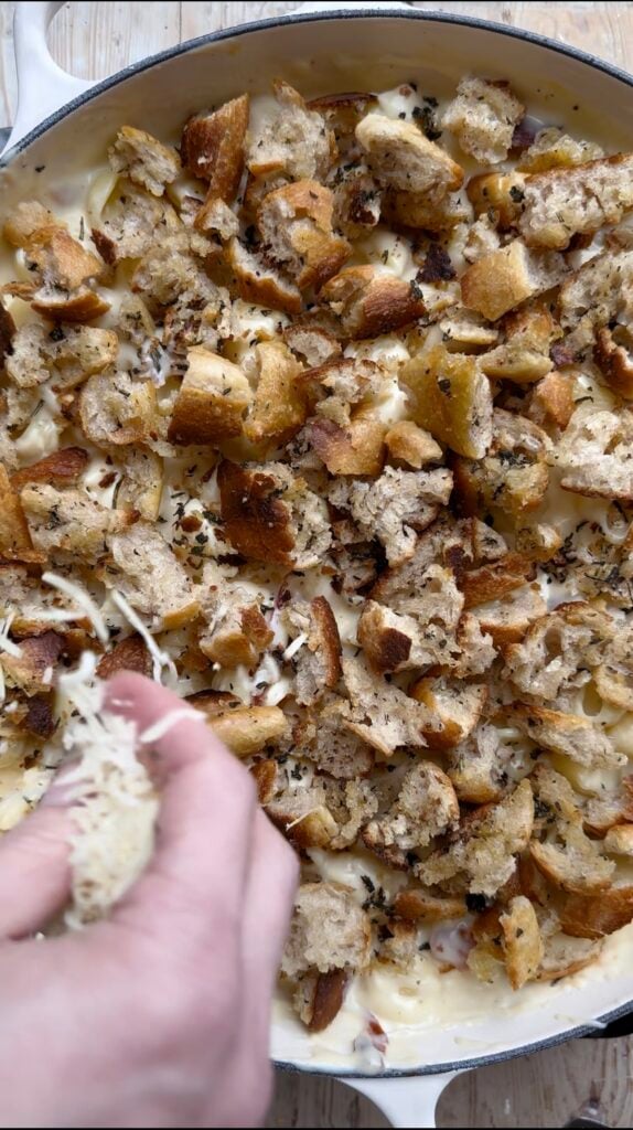 Hand sprinkling cheese over a crouton topped casserole.