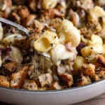 A spoon scooping cheesy noodles from a baked casserole dish.