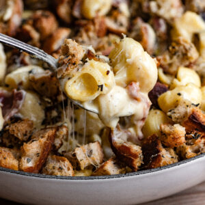 A spoon scooping cheesy noodles from a baked casserole dish.