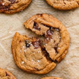 Closeup of a toffee cookie broken in half on a piece of parchment paper.
