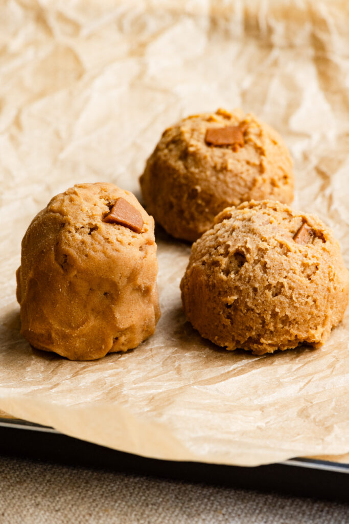 A tall cookie dough mound next to round cookie dough scoops on parchment paper.