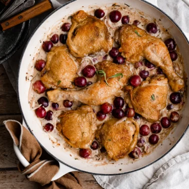 Overhead of a skillet filled with cooked chicken thighs and grapes in a cream sauce.