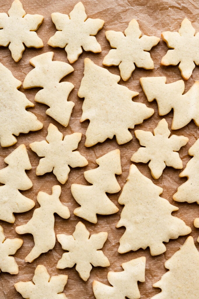 Baked sugar cookies in tree, snowflake, and deer shapes on parchment paper.