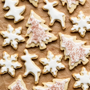 Overhead of frosted sugar cookies cutout in tree, snowflake, and deer shapes on parchment paper.