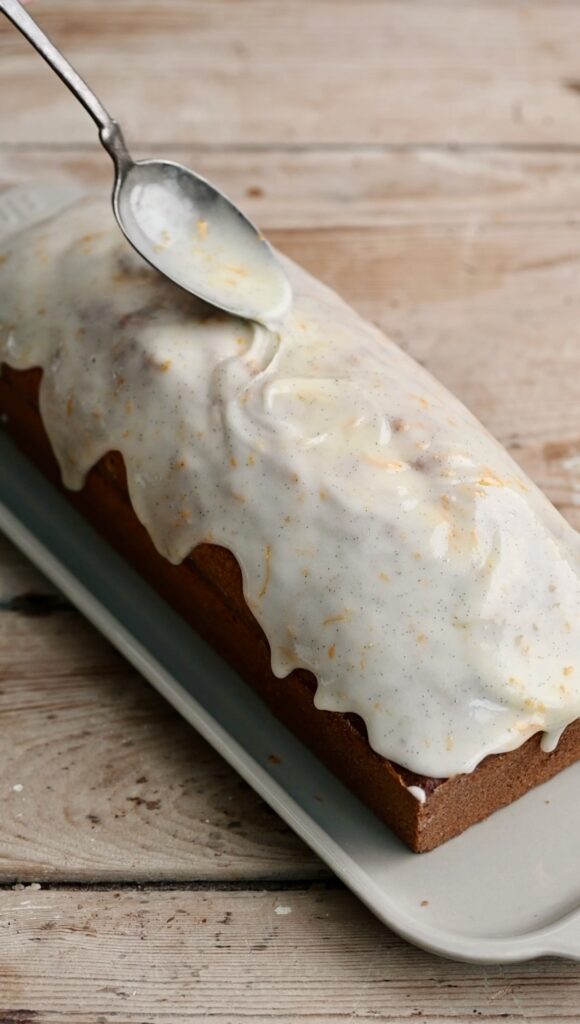 Orange cake glaze being spooned over a loaf cake.