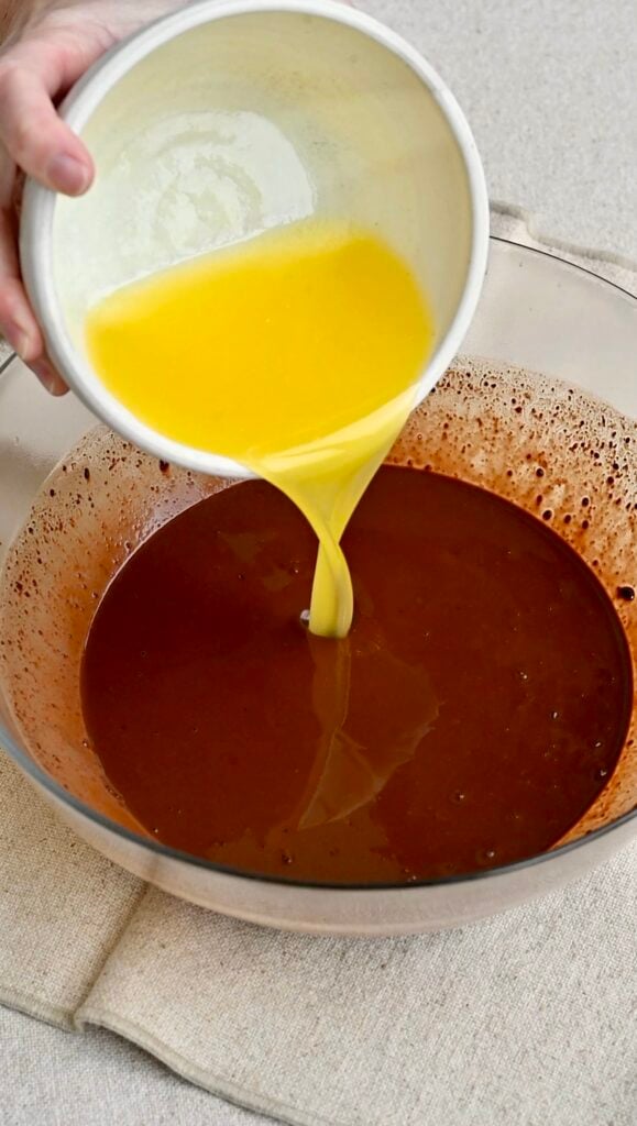 Melted butter pouring into a bowl of liquid chocolate.