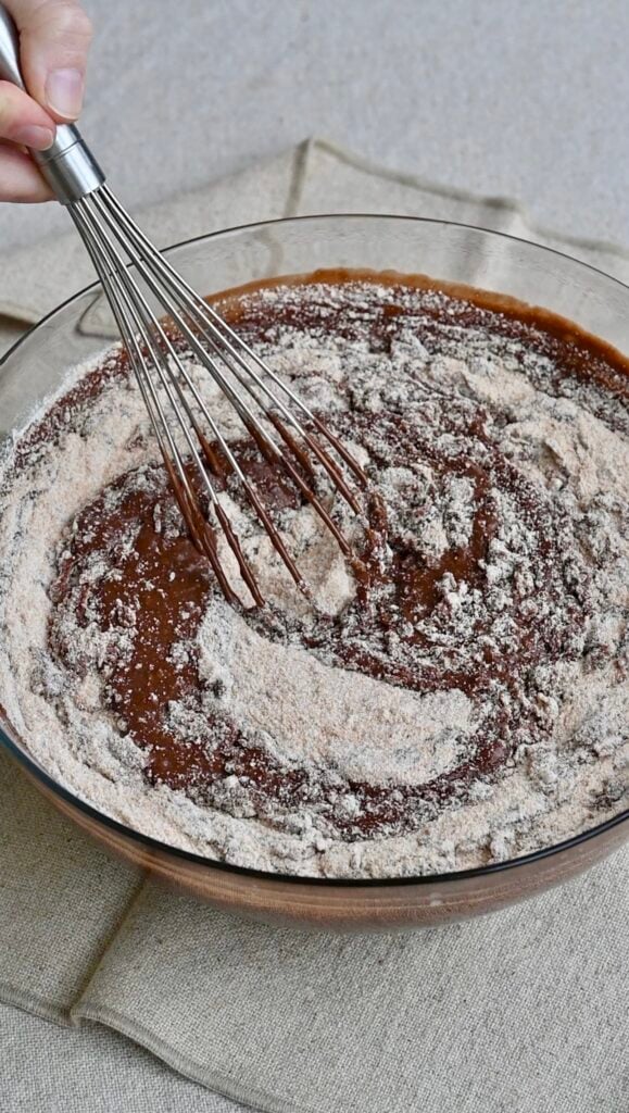Flour and sugar being whisked into a chocolate mixture.
