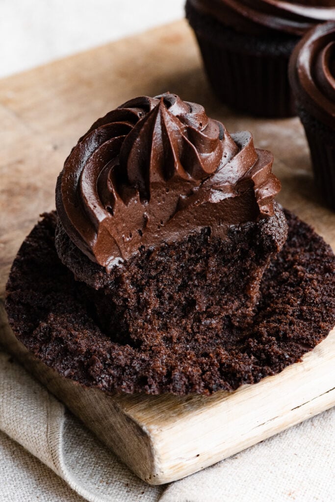 Half of a frosted dark chocolate cupcake sitting on a cupcake wrapper.