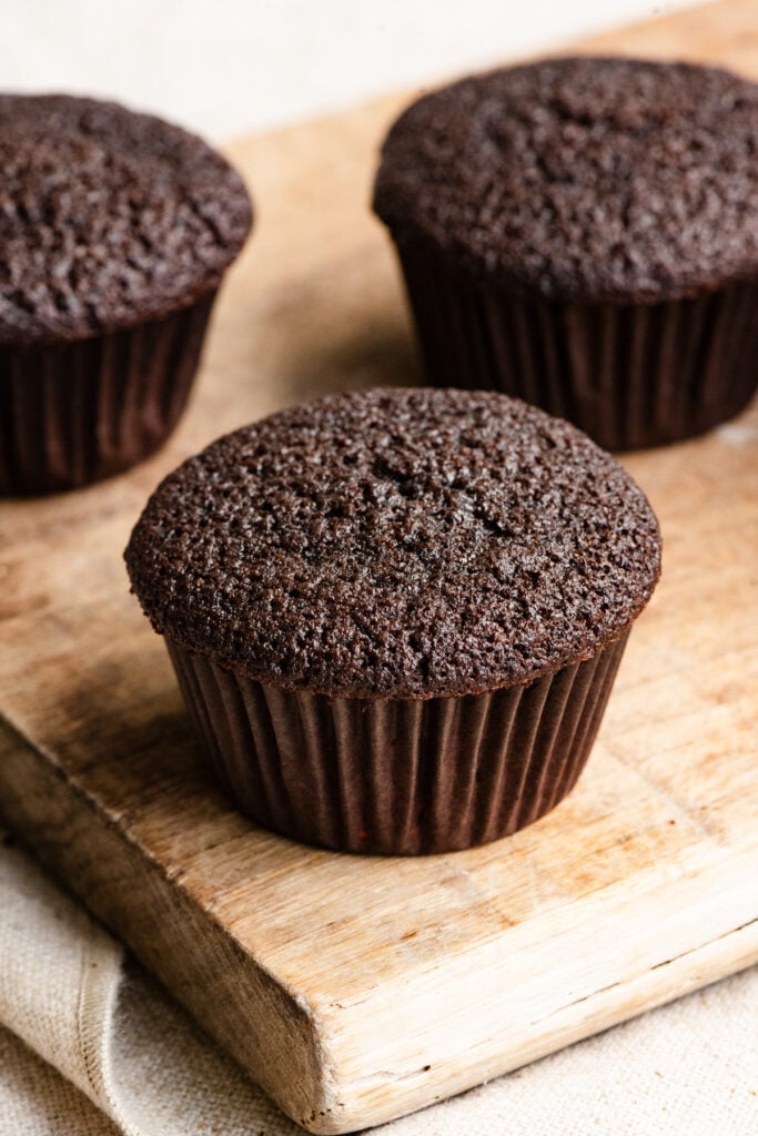 Baked dark chocolate cupcakes on a wooden cutting board.