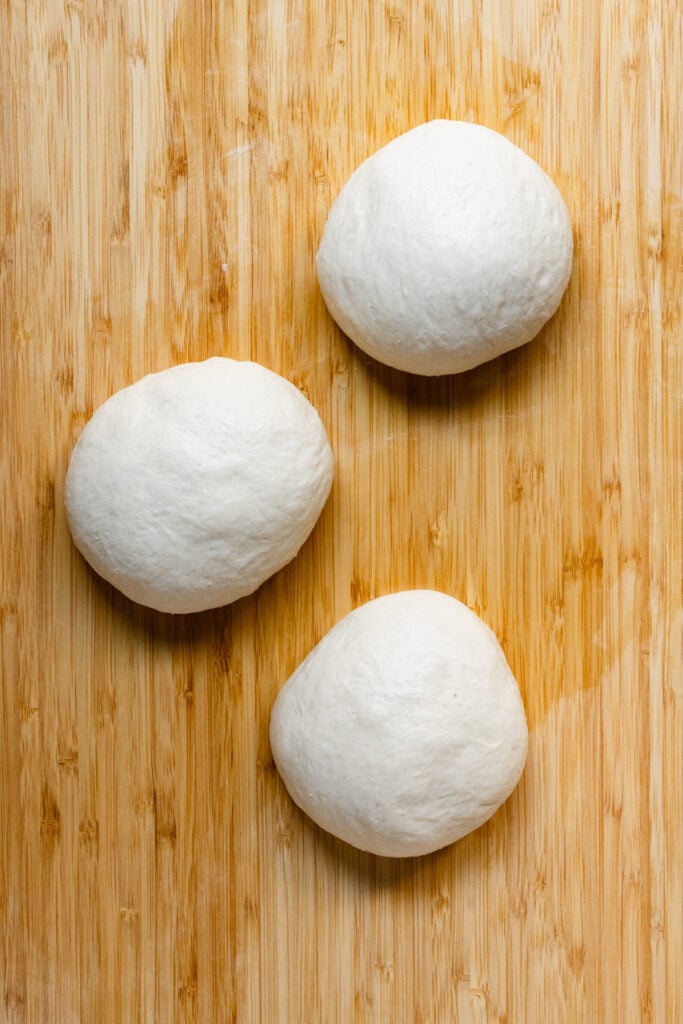 Three pizza dough balls on a kitchen wood countertop.