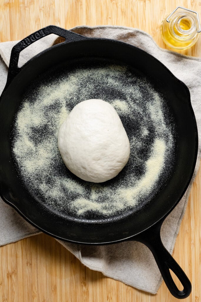 A ball of pizza dough in the center of a cast iron skillet.