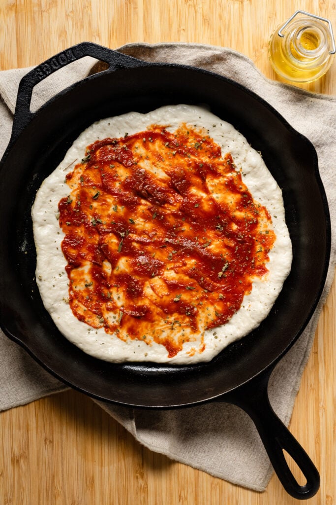 Overhead of tomato sauce spread onto pan pizza dough.