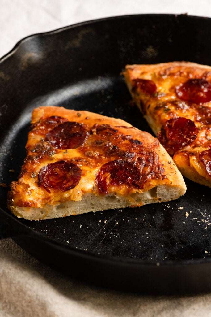 Slice of pepperoni pan pizza in a cast iron skillet.