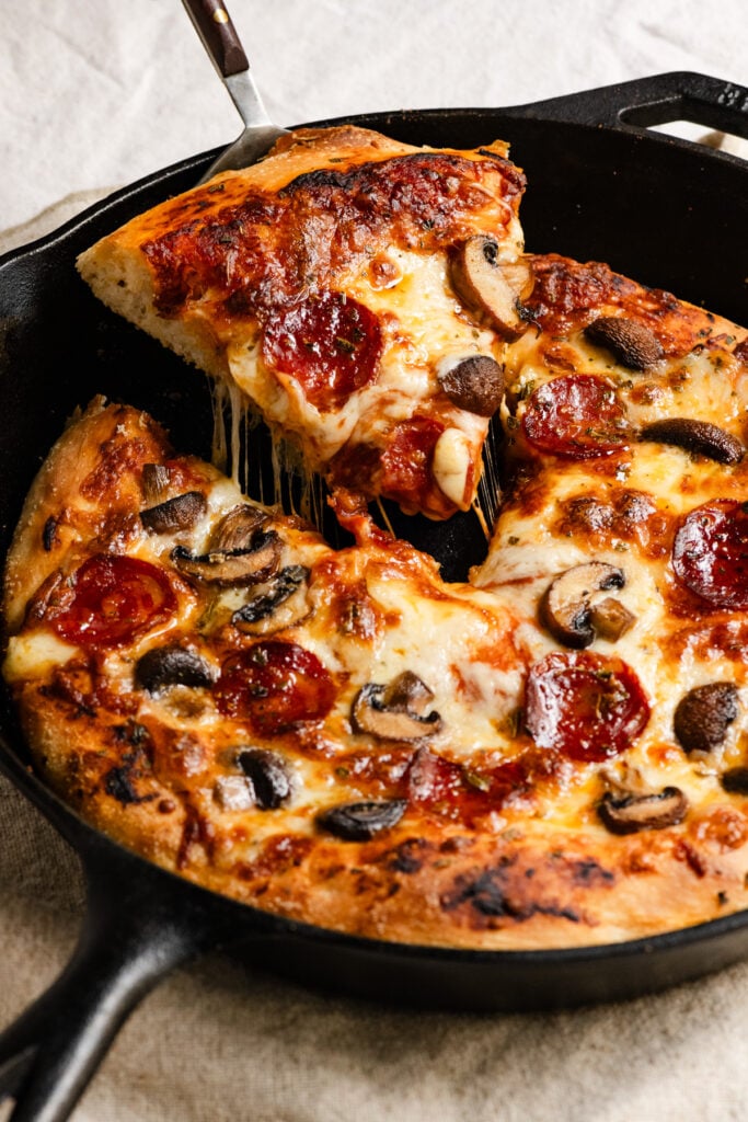 Slice of pizza being pulled from a pizza in a cast iron skillet.