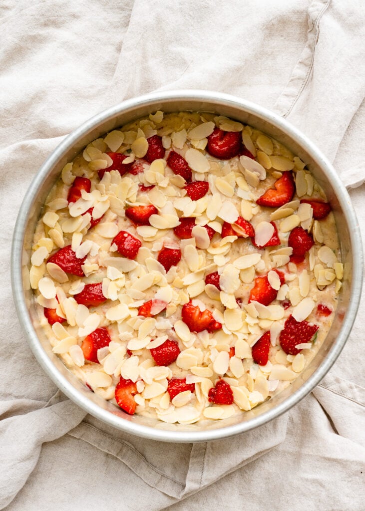Overhead of strawberry cake batter on cake pan topped with almond slices.