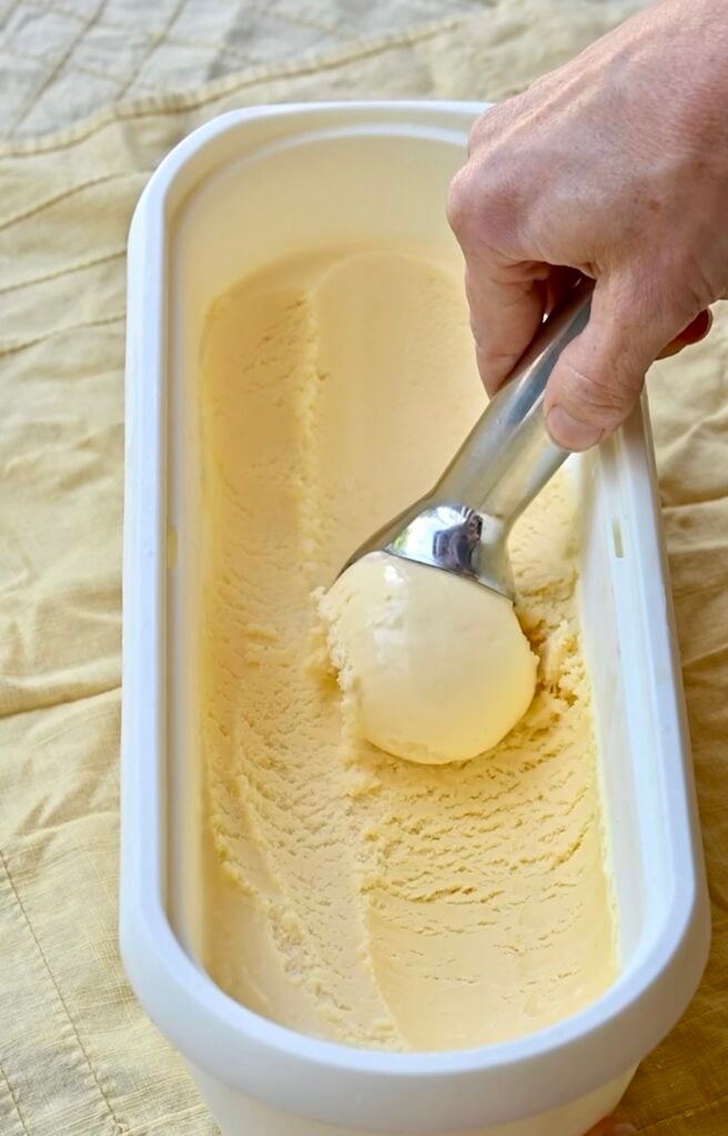 Hand scooping lemon ice cream from a container,