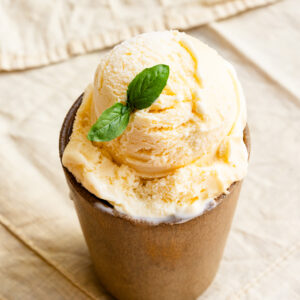 Scoop of lemon ice cream in a cup with a basil leaf.