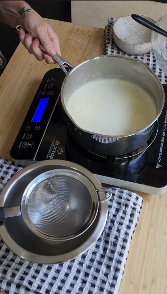 Heavy cream in a pot next to a bowl fitted with a metal seive.