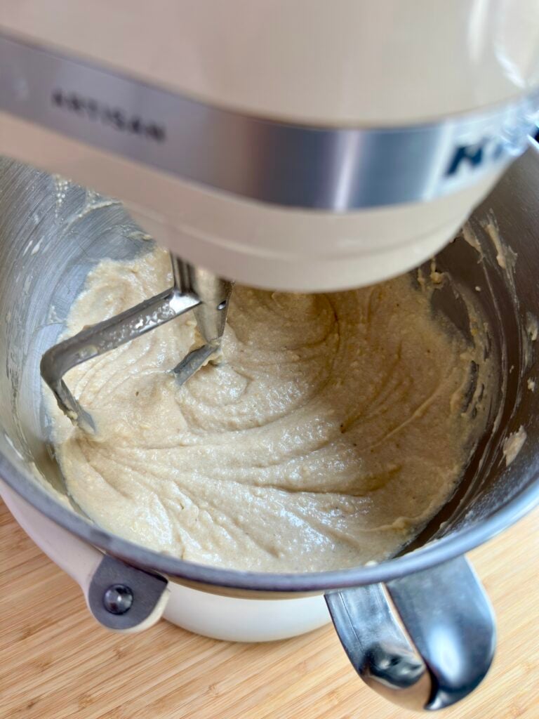 Banana cake batter being mixed in a stand mixer with paddle attachment.