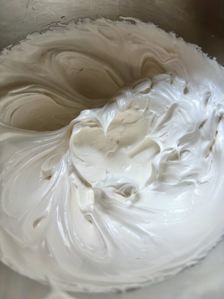 Meringue with stiff peaks in the bottom of a mixing bowl.